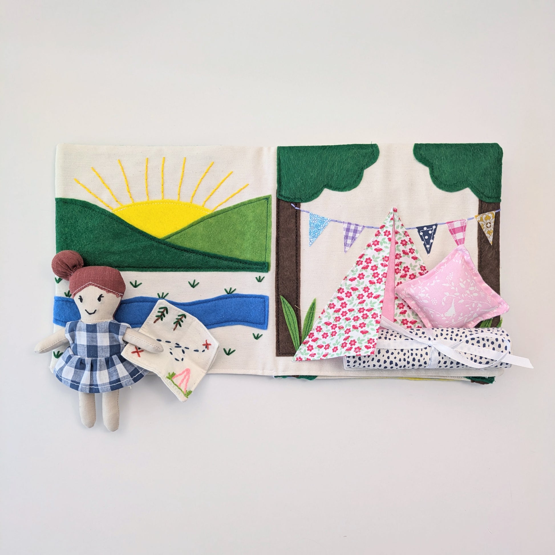 Fabric book with a landscape scene, doll, and clothes on a white background