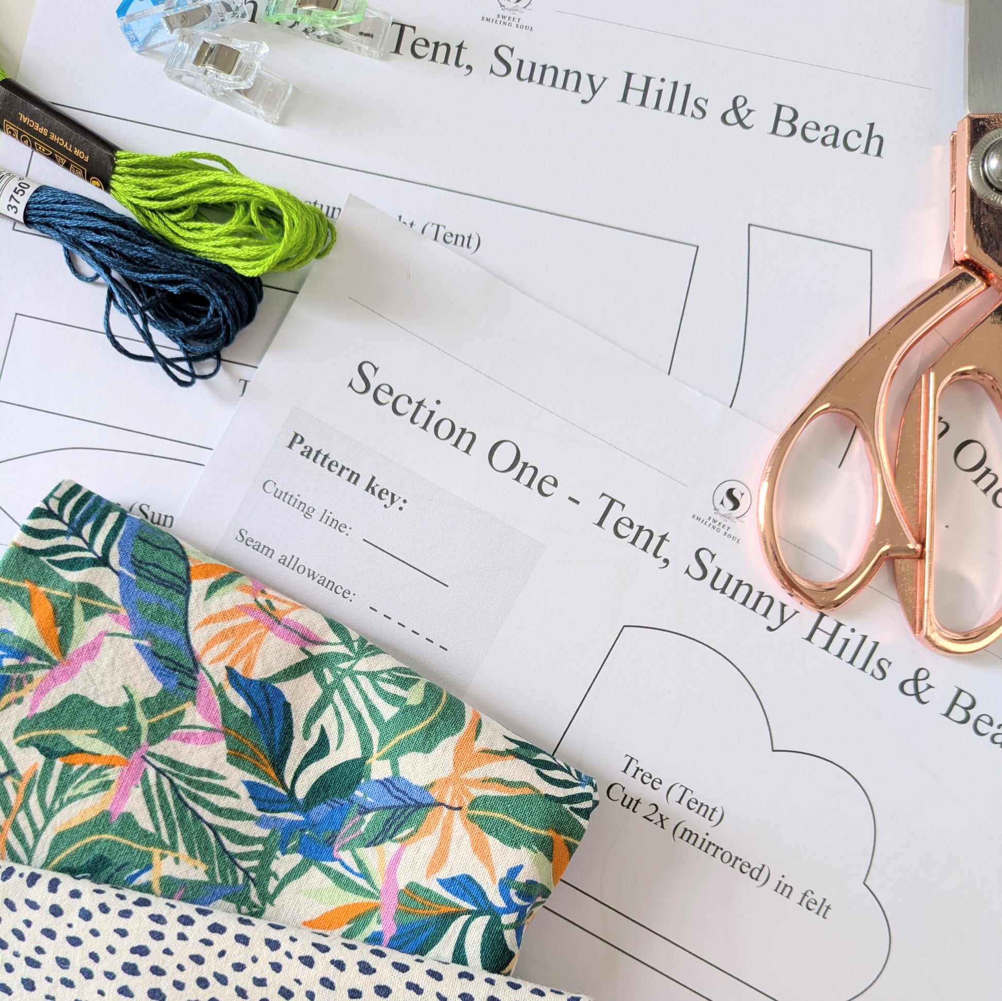Floral fabric, scissors, and thread on a pattern sheet for a tent design.