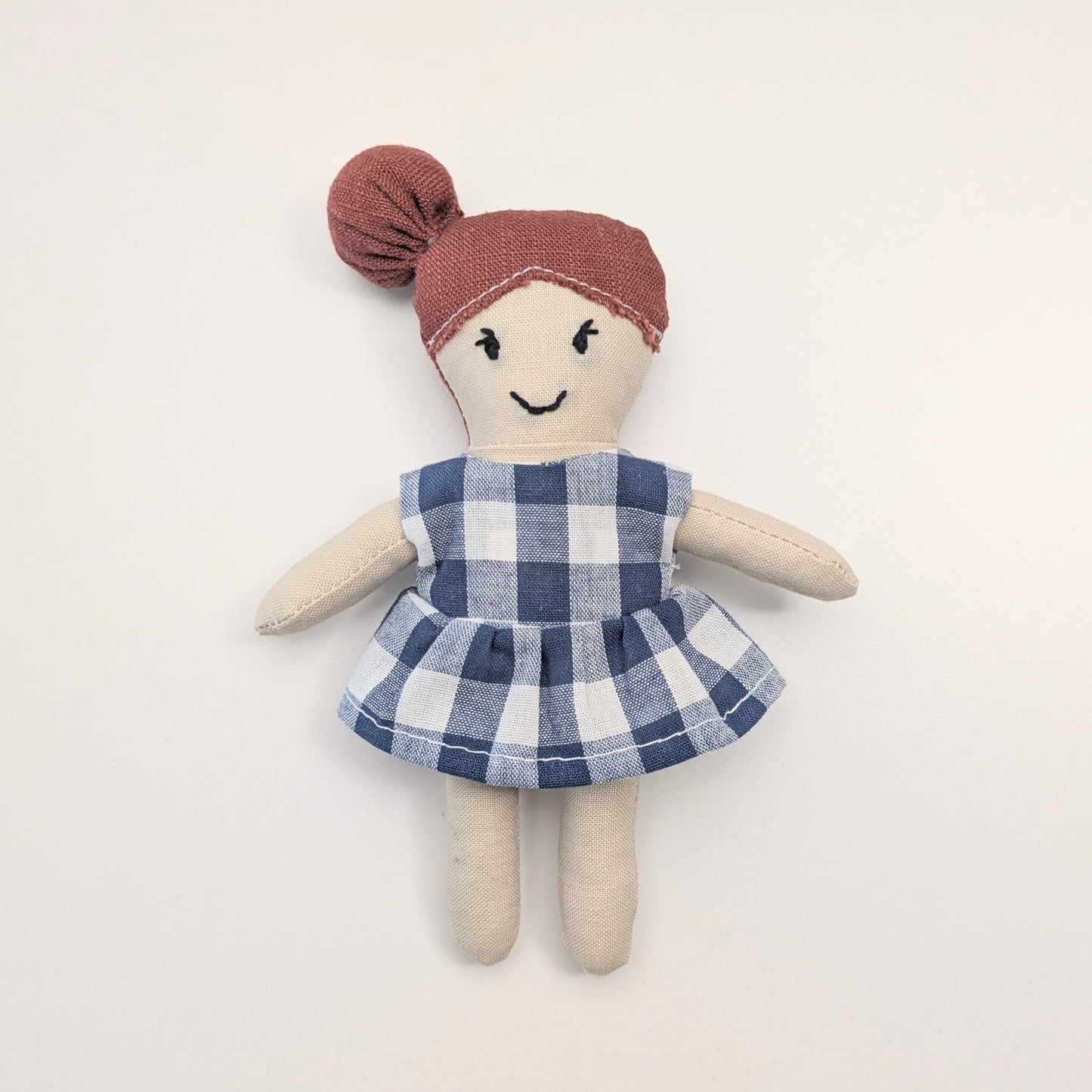 Toy doll with a blue checkered dress and red headband on a light background
