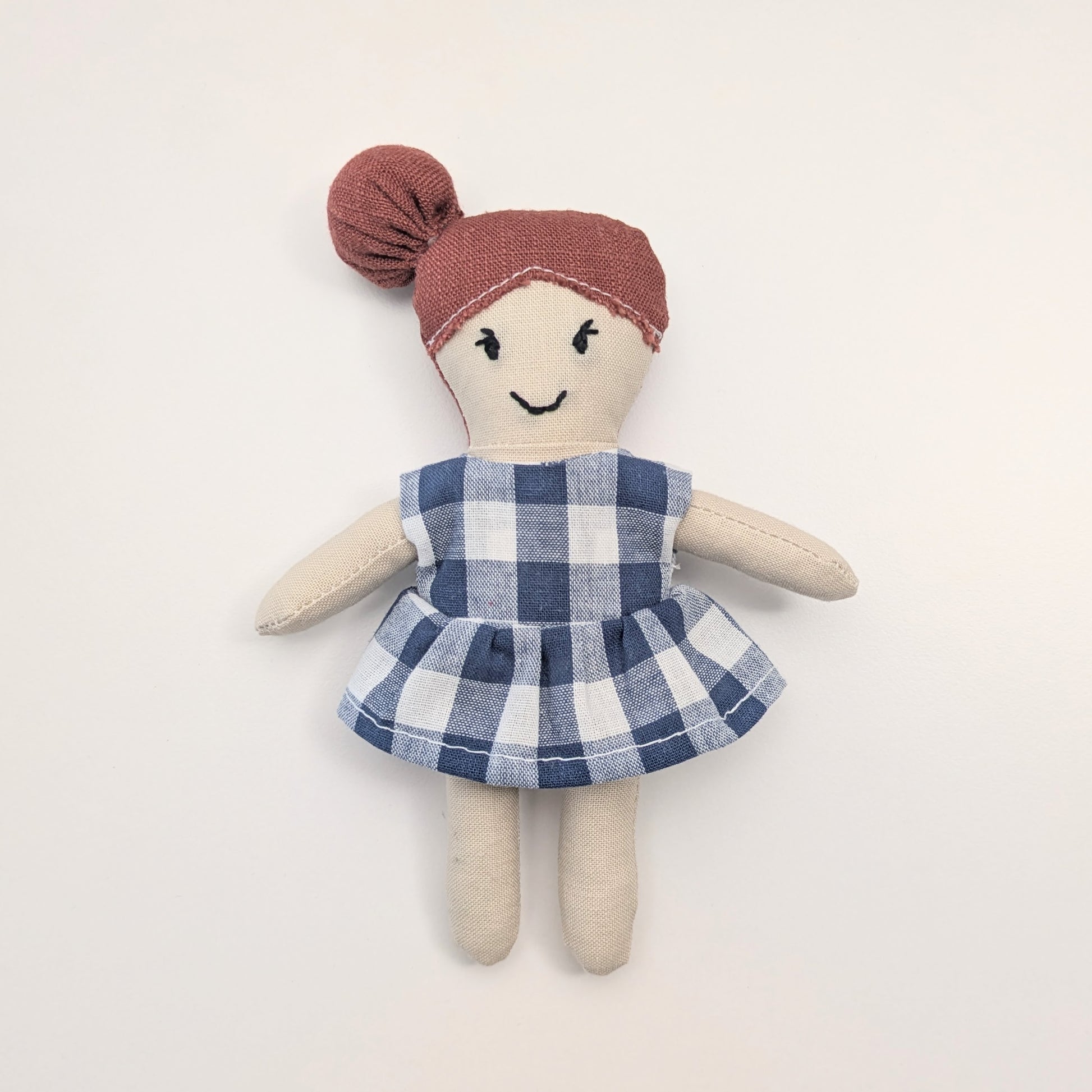 Toy doll with a blue checkered dress and red headband on a light background