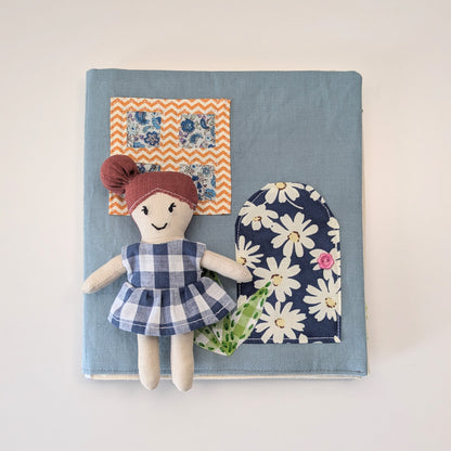 Small fabric doll with a checkered dress on a blue background with floral and zigzag patterns.